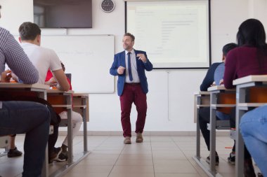 Erkek profesör öğrencilere ders veriyor ve onlarla iletişim kuruyor.