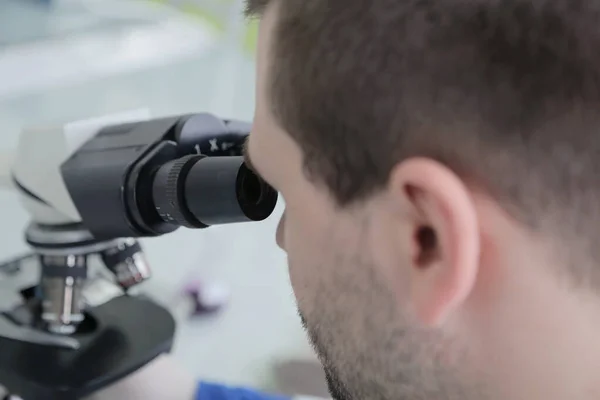 Cientista masculino novo que olha através de um microscópio em um labo — Fotografia de Stock