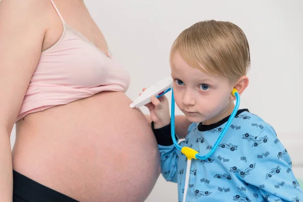 Escuchando el tummy. Curioso chico de ojos oscuros que se siente muy bien. — Foto de Stock