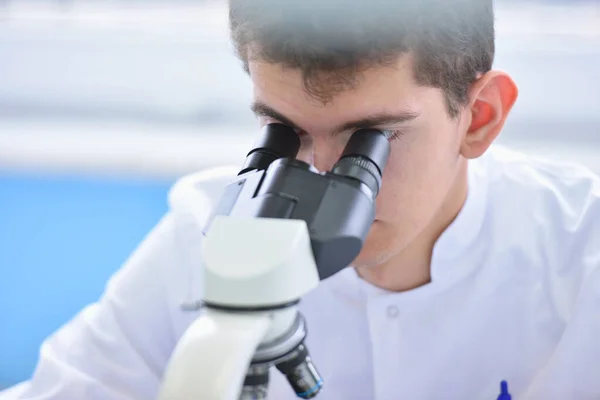 Νεαρός επιστήμονας που κοιτάζει μέσα από ένα μικροσκόπιο σε ένα εργαστήριο — Φωτογραφία Αρχείου