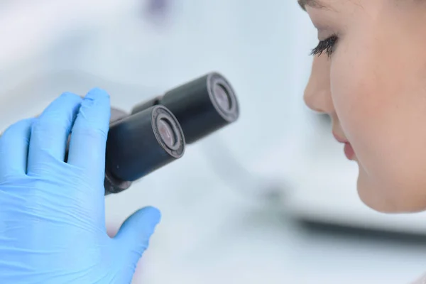 Jovem cientista do sexo feminino olhando através de um microscópio em um la — Fotografia de Stock