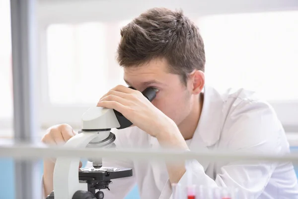 Jonge mannelijke wetenschapper kijkt door een microscoop in een laborator — Stockfoto