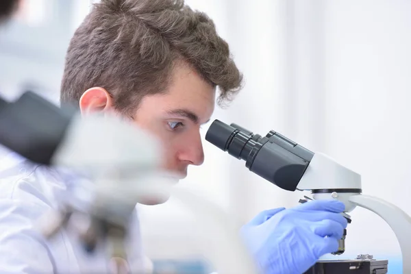 Joven científico masculino mirando a través de un microscopio en un laboratorio — Foto de Stock