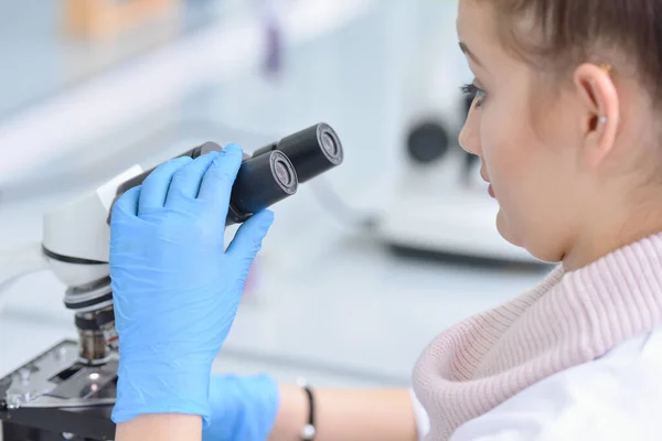 Νεαρή γυναίκα επιστήμονας που κοιτάζει μέσα από ένα μικροσκόπιο στο a la — Φωτογραφία Αρχείου