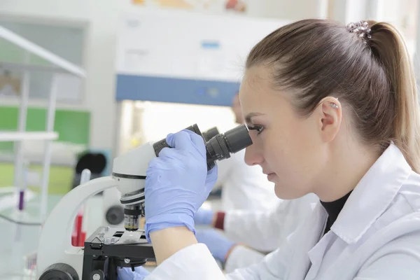 Jeune femme scientifique regardant à travers un microscope dans un laboratoire — Photo