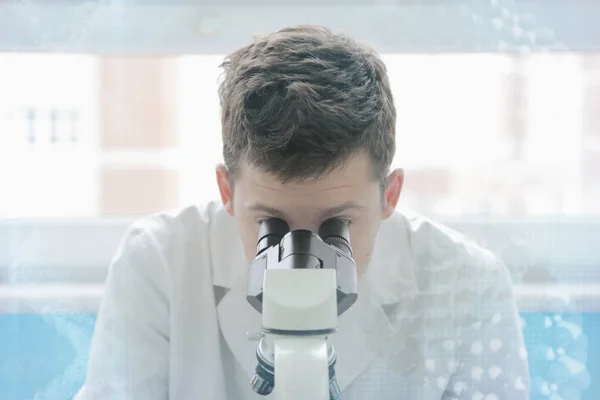 Young male male scientist looking through a microscope in a labo — Stock Photo, Image