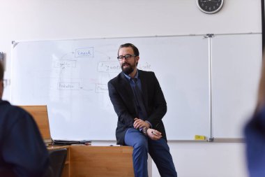 Erkek profesör öğrencilere ders veriyor ve onlarla iletişim kuruyor.