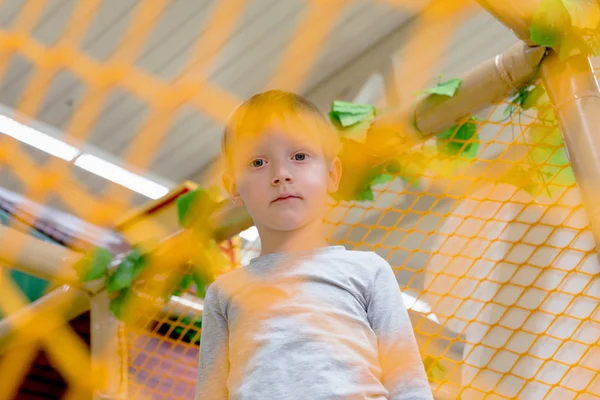 Kid spelen op nieuwe speeltuin kleuterschool achter het net. — Stockfoto