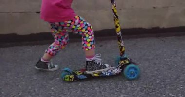 Küçük çocuk güneşli bir yaz gününde şehir parkında scooter sürmeyi öğreniyor. Patenli tatlı anaokulu kızı.. 
