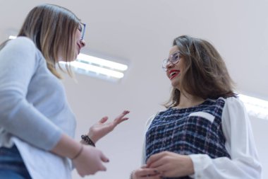 İki çalışkan öğrenci kız güneşli kütüphanede sohbet ediyorlar..