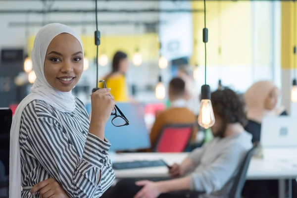 Muslim business lady wearing hijab and working at computer in office. Pretty african woman in hijab looking at camera and smiling. Concept of workplace and multiethnic relations