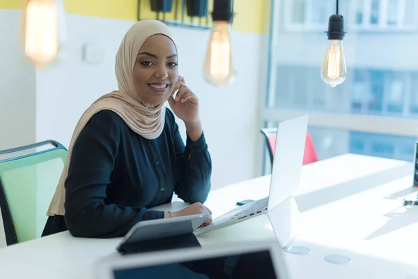 Muslim business lady wearing hijab and working at computer in office. Pretty african woman in hijab looking at camera and smiling. Concept of workplace and multiethnic relations