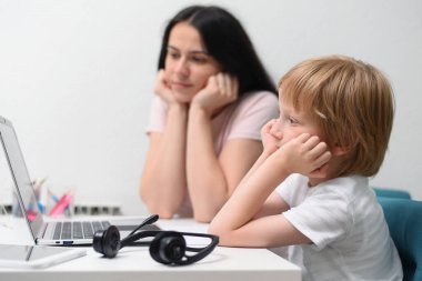 Coronavirus salgını. Kilitlenme ve okul kapanması. Anne, oğlunun evde online ders çalışmasına yardım ediyor. COVID-19 salgını çocukları ve öğretmenleri çevrimiçi öğrenmeye zorluyor.