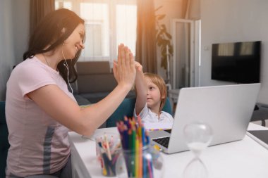 Coronavirus salgını. Kilitlenme ve okul kapanması. Anne, oğlunun evde online ders çalışmasına yardım ediyor. COVID-19 salgını çocukları ve öğretmenleri çevrimiçi öğrenmeye zorluyor.