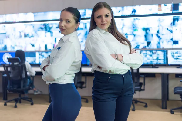 Security guard monitoring modern CCTV cameras in surveillance room. Two Female security guard in surveillance room. Smiling into camera and posing.
