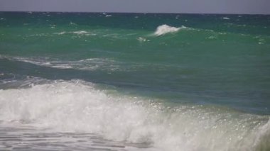Mavi-yeşil Akdeniz 'de güçlü bir rüzgar esiyor ve dalgalar kumsala vuruyor, ağır çekimde.
