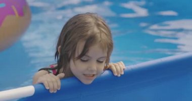 Küçük kız bahçedeki şişme yüzme havuzunda oynuyor. 