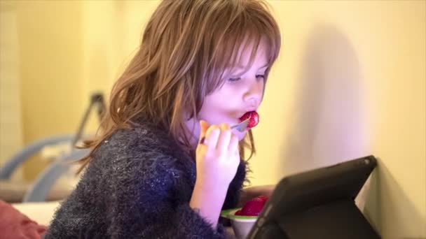 可爱的小女孩在客厅里吃草莓 看平板电脑 — 图库视频影像