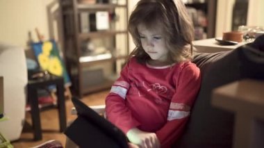 Pijama giymiş, geceleri oturma odasında tablet izleyen sevimli küçük bir kız..