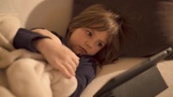 Красивая Маленькая Девочка Лежит Диване Гостиной Смотрит Планшет — стоковое видео