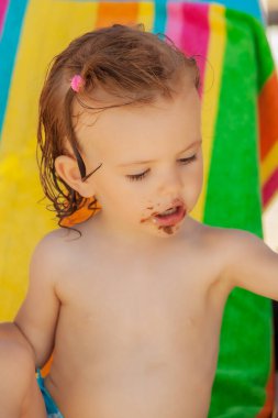 Bebek, kumsalda çikolatalı çörek yiyor. Sahada sığ bir derinlik var.
