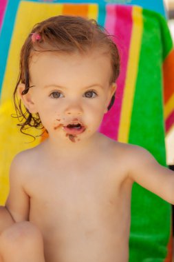Bebek, kumsalda çikolatalı çörek yiyor. Sahada sığ bir derinlik var.