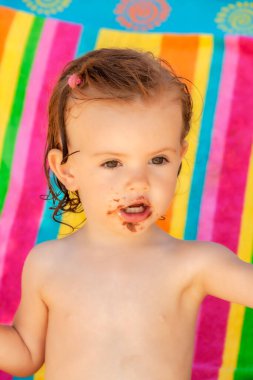 Bebek, kumsalda çikolatalı çörek yiyor. Sahada sığ bir derinlik var.