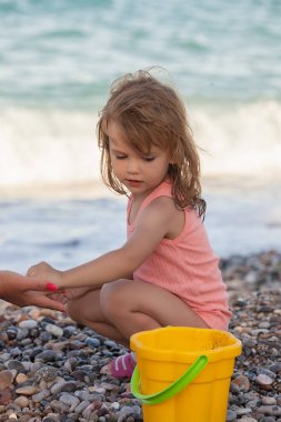 Sahilde çakıl taşlarıyla oynayan küçük bir kız.