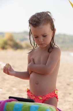 Küçük kız kumsalda kurabiye yiyor, tarlanın derinliğine dikkat et.