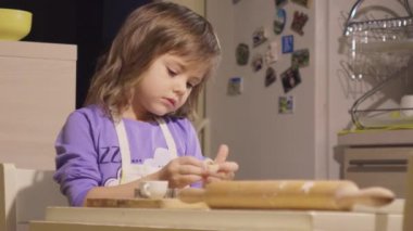 Sevimli küçük kız annesiyle mutfak masasında bisküvi yapıyor.