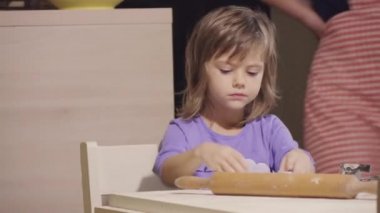 Sevimli küçük kız annesiyle mutfak masasında bisküvi yapıyor.