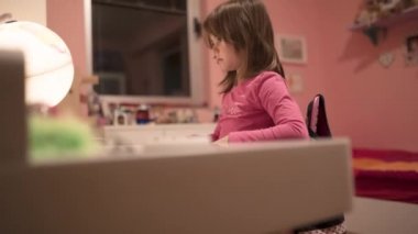 Okul masasında aydınlanmış bir küreyle resim çizen ve tablet izleyen sevimli küçük kız, seçici bir odak noktası.