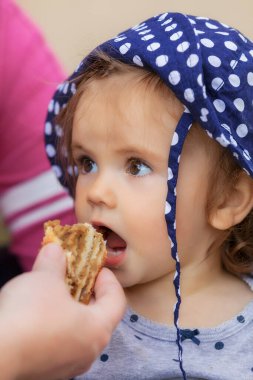 Çocuk kafasında nokta olan bir şapkayla bisküvi yiyor, alanın derinliğine dikkat edin.