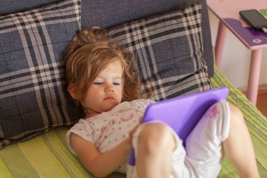 Küçük kız yatakta yatar ve dizüstü bilgisayarda çizgi film seyreder.