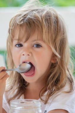 Küçük kız kaşıkla bal yiyor.