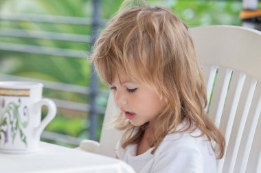 Terasta kahvaltı ederken küçük bir kızın portresi, tarlanın sığ derinliğine dikkat edin.