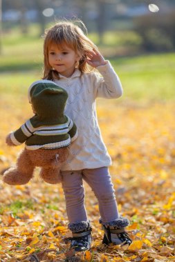 Ayısıyla sonbahar yapraklarında yürüyen küçük kız.