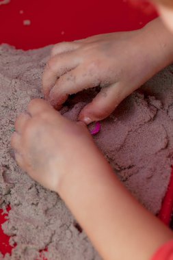 Kırmızı trenin üzerinde küçük eller kinetik kumla ve kalıplarla oynuyor.