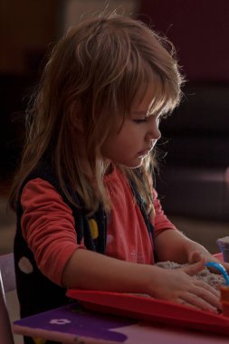 Küçük kız kinetik kum ve kalıplarla oynuyor.