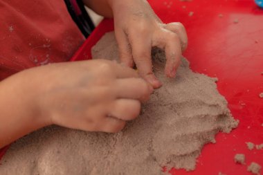 Küçük eller kırmızı tepside kinetik kum ve kalıplarla oynuyorlar.