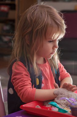 Küçük kız kinetik kum ve kalıplarla oynuyor.