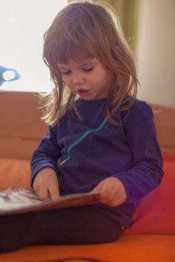 Evdeki yatakta kitap okuyan küçük bir kız.