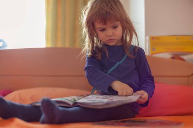 Evdeki yatakta kitap okuyan küçük bir kız.