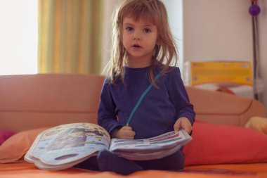 Evdeki yatakta kitap okuyan küçük bir kız.