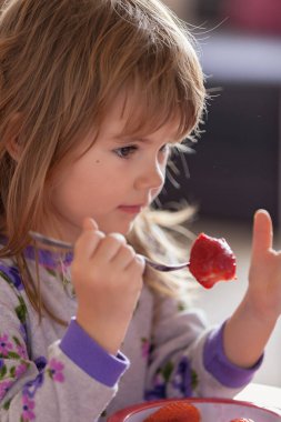 Çocuk kahvaltıdan sonra evde pijamalarıyla çilek yiyor.
