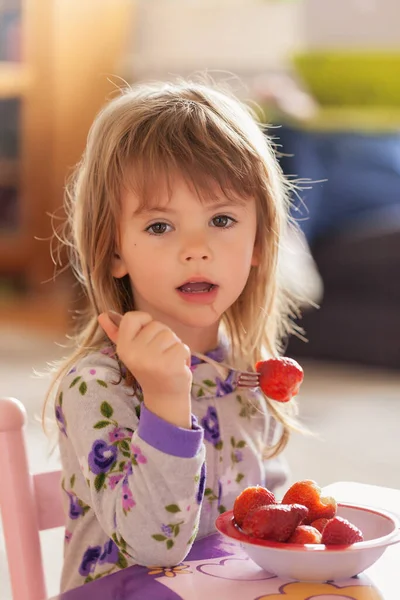 Çocuk kahvaltıdan sonra evde pijamalarıyla çilek yiyor.