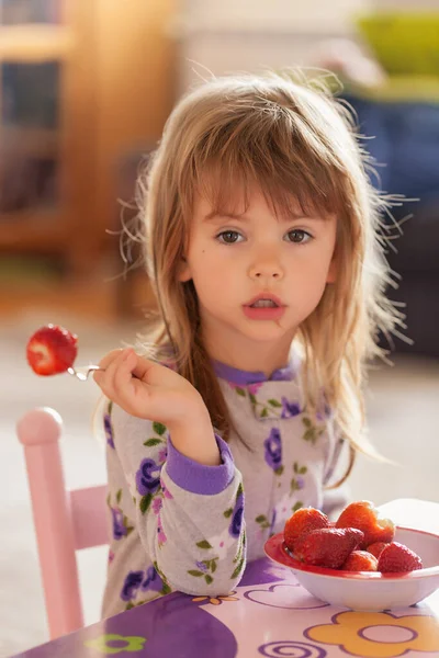 Çocuk kahvaltıdan sonra evde pijamalarıyla çilek yiyor.