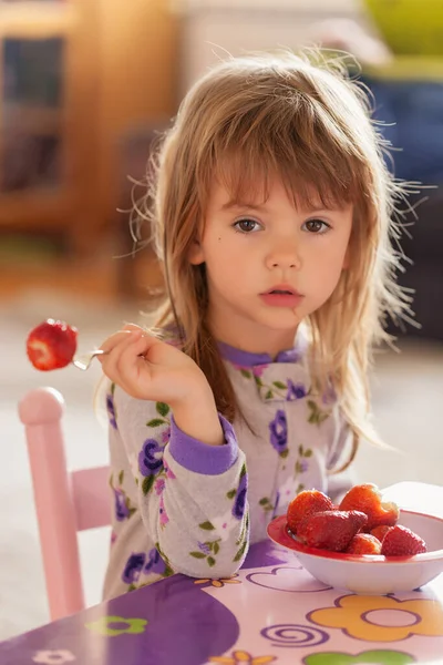 Çocuk kahvaltıdan sonra evde pijamalarıyla çilek yiyor.