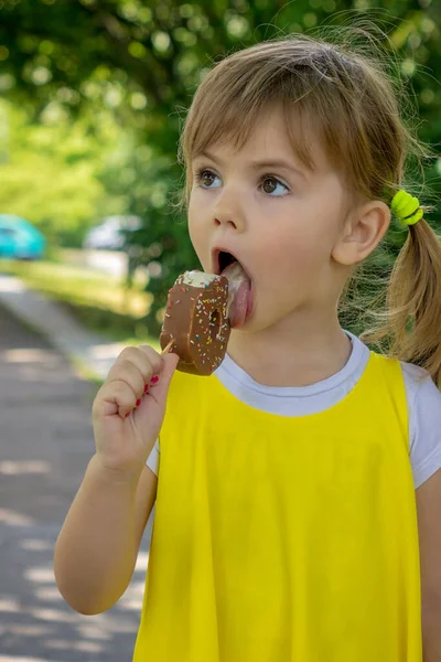 黄色のドレスを着た少女が自然の中でアイスクリームを舐めています ロイヤリティフリーのストック画像