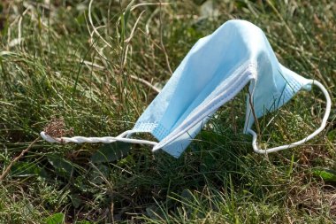 Çimlerin üzerinde mavi yüz maskesi kullanılmış. Yüz maskesi yanlış kurtulmuş. Doğa kirliliği ve çevre felaketi. Covid-19 salgını.